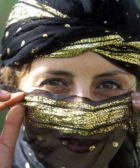 Woman with a decorative black and gold headscarf partially covering her face, revealing her eyes. - Olive Oil Times