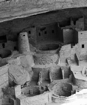 Black and white image of an ancient cliff dwelling with circular and rectangular structures. - Olive Oil Times