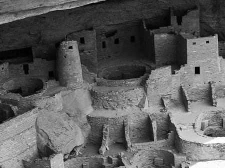 Black and white image of an ancient cliff dwelling with circular and rectangular structures. - Olive Oil Times