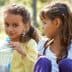 Two young girls sitting outdoors, one holding a plastic water bottle and looking at the other. - Olive Oil Times