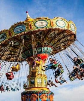 Colorful swing ride with multiple seats and riders at an amusement park against a blue sky. - Olive Oil Times