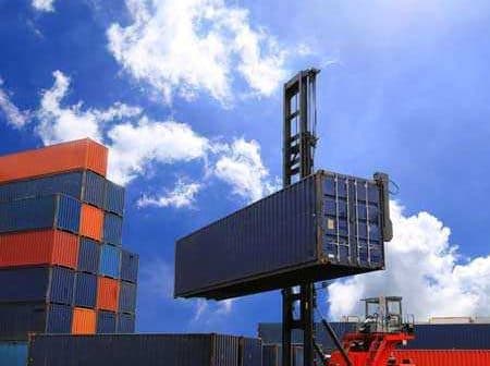Red forklift lifting a blue shipping container at a cargo yard with stacked containers in the background. - Olive Oil Times