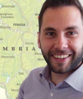 Man with a beard smiling in front of a map of Umbria, Italy, showing various towns and geographical features. - Olive Oil Times