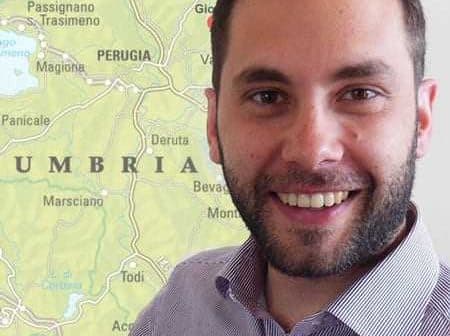 Man with a beard smiling in front of a map of Umbria, Italy, showing various towns and geographical features. - Olive Oil Times