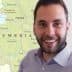 Man with a beard smiling in front of a map of Umbria, Italy, showing various towns and geographical features. - Olive Oil Times