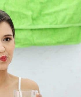 A woman rinsing her mouth with water while looking in a mirror in a bathroom. - Olive Oil Times