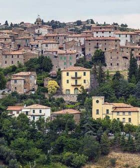 A scenic view of a Tuscan village with stone buildings and terracotta roofs surrounded by greenery. - Olive Oil Times