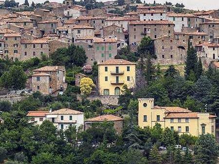 A scenic view of a Tuscan village with stone buildings and terracotta roofs surrounded by greenery. - Olive Oil Times