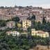 A scenic view of a Tuscan village with stone buildings and terracotta roofs surrounded by greenery. - Olive Oil Times