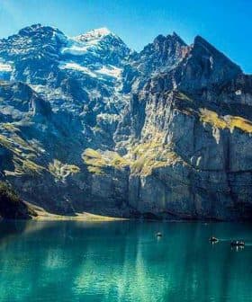 Scenic view of a mountain landscape with a clear blue lake in the foreground and rocky peaks in the background. - Olive Oil Times