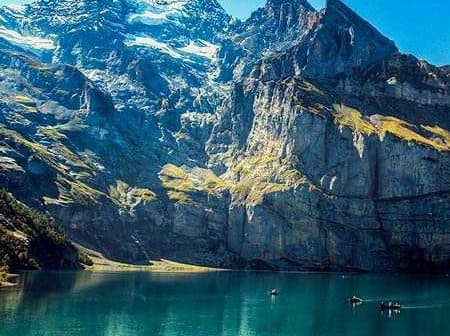Scenic view of a mountain landscape with a clear blue lake in the foreground and rocky peaks in the background. - Olive Oil Times