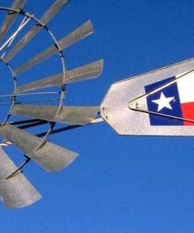 Close-up of a windmill with a Texas state flag attached to its arm against a blue sky. - Olive Oil Times