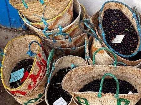 Several woven baskets filled with black olives, some labeled with tags, arranged together. - Olive Oil Times