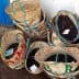 Several woven baskets filled with black olives, some labeled with tags, arranged together. - Olive Oil Times