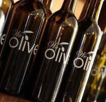 Several dark glass bottles with a label that reads 'We Olive' displayed in a row. - Olive Oil Times