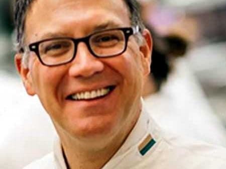 Chef wearing a white uniform and glasses, smiling at the camera in a kitchen setting. - Olive Oil Times