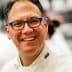 Chef wearing a white uniform and glasses, smiling at the camera in a kitchen setting. - Olive Oil Times