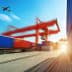 Cargo containers stacked at a shipping port with an airplane flying overhead in a clear sky. - Olive Oil Times