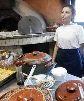 Woman standing in a kitchen with various cooking pots and an oven in the background. - Olive Oil Times