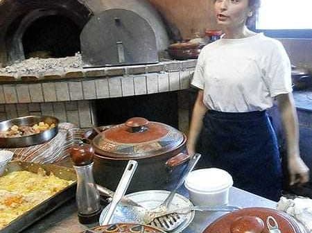 Woman standing in a kitchen with various cooking pots and an oven in the background. - Olive Oil Times