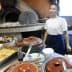 Woman standing in a kitchen with various cooking pots and an oven in the background. - Olive Oil Times