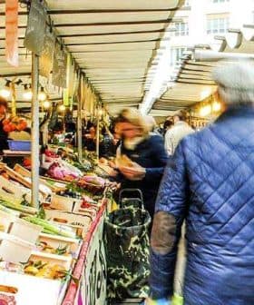 Busy market scene featuring various stalls with fresh produce and shoppers walking through the aisles. - Olive Oil Times