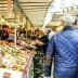 Busy market scene featuring various stalls with fresh produce and shoppers walking through the aisles. - Olive Oil Times