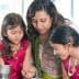 A woman and two girls engaged in cooking together, wearing traditional attire in a kitchen setting. - Olive Oil Times