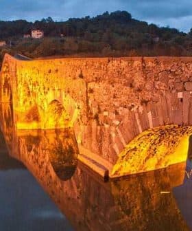 Stone bridge illuminated by warm light, reflecting in calm water during twilight. - Olive Oil Times