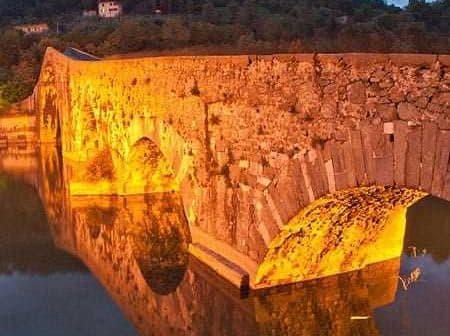 Stone bridge illuminated by warm light, reflecting in calm water during twilight. - Olive Oil Times
