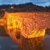 Stone bridge illuminated by warm light, reflecting in calm water during twilight. - Olive Oil Times