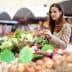 A woman examining fresh vegetables at a market stall filled with various produce. - Olive Oil Times