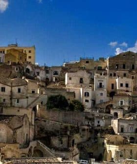 A view of historic stone buildings stacked on a hillside in Matera, Italy under a blue sky. - Olive Oil Times