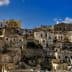 A view of historic stone buildings stacked on a hillside in Matera, Italy under a blue sky. - Olive Oil Times