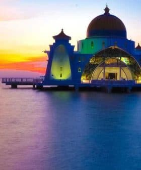 A mosque with a golden dome and colorful lighting situated by the water during sunset. - Olive Oil Times