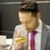 Man in a suit holding a glass of olive oil and smelling it at an event. - Olive Oil Times