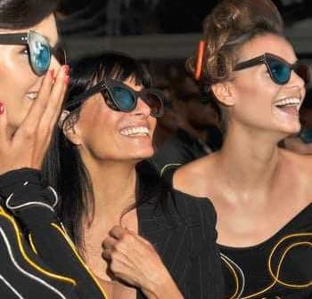 Three women smiling and wearing sunglasses at an event, showcasing various styles of eyewear. - Olive Oil Times
