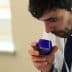 A man holding a blue glass with 'NYIOOC' while smelling its contents during an olive oil tasting. - Olive Oil Times