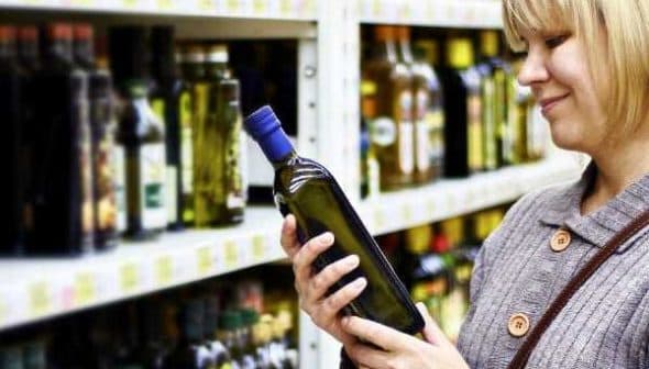 Woman holding and examining a bottle of olive oil in a grocery store aisle. - Olive Oil Times