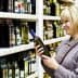 Woman holding and examining a bottle of olive oil in a grocery store aisle. - Olive Oil Times