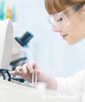 Female scientist in a lab coat and safety glasses operating laboratory equipment with test tubes. - Olive Oil Times