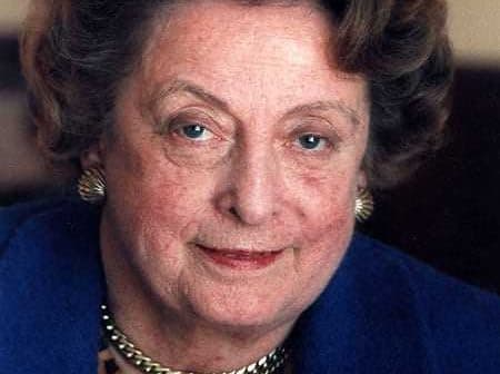 Close-up portrait of a woman with curly hair and blue eyes wearing a blue jacket. - Olive Oil Times