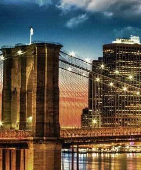 Brooklyn Bridge with illuminated towers and city skyline during sunset. - Olive Oil Times