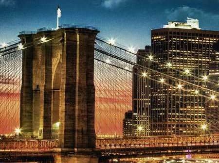 Brooklyn Bridge with illuminated towers and city skyline during sunset. - Olive Oil Times