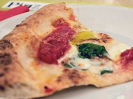A slice of pizza topped with tomato sauce, cheese, spinach, and a yellow pepper on a white plate. - Olive Oil Times