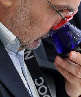 Man with glasses smelling olive oil from a blue tasting glass during an evaluation. - Olive Oil Times