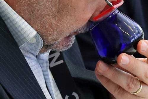 Man with glasses smelling olive oil from a blue tasting glass during an evaluation. - Olive Oil Times