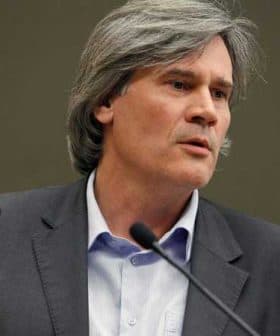 A man with gray hair speaking at a podium during a presentation or conference. - Olive Oil Times