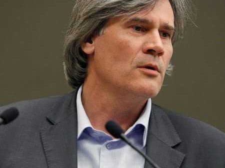 A man with gray hair speaking at a podium during a presentation or conference. - Olive Oil Times