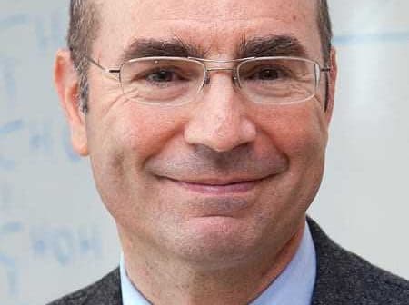 A man wearing glasses and a gray suit, smiling at the camera with a neutral background. - Olive Oil Times